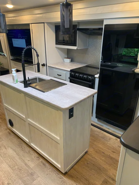 Modern RV rental kitchen with island sink, sleek appliances, and a TV. Bright interior design ideal for comfortable travel.. Forest River Vibe 2023