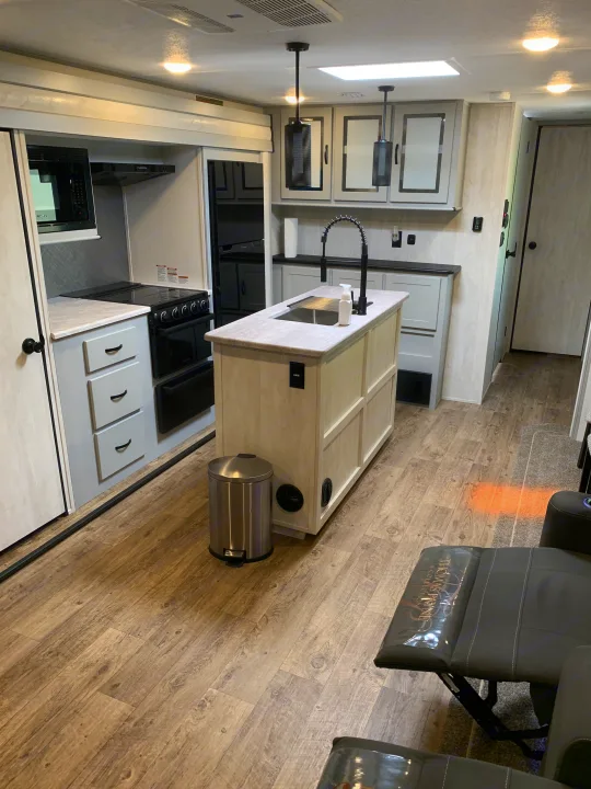 Step inside this modern RV rental: a bright kitchen with an island, black appliances, and cozy recliners for a comfortable journey.. Forest River Vibe 2023