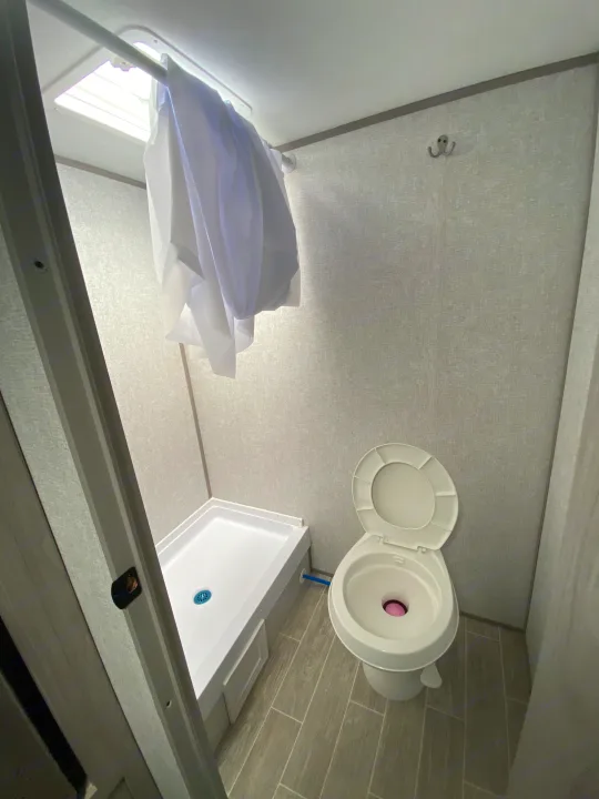 This RV rental bathroom showcases a white shower and toilet in a compact space. Natural light enters from a ceiling skylight.. Dutchmen Coleman Lantern LT 2022