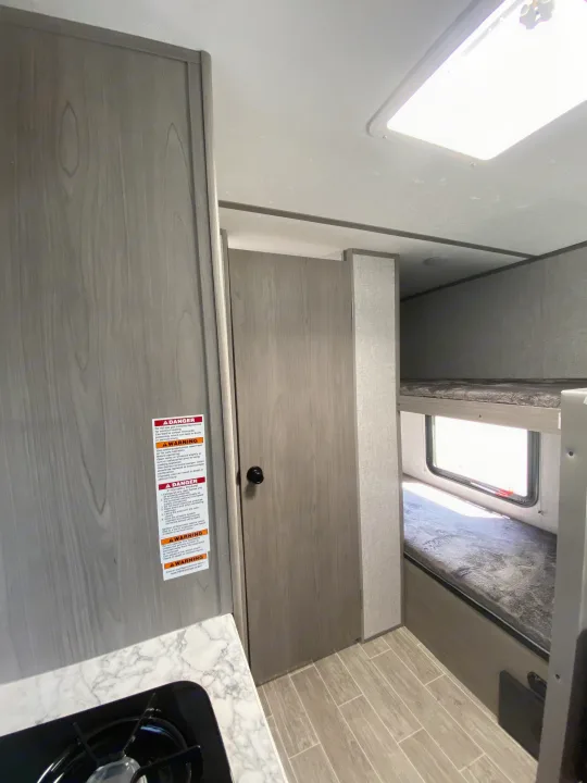 Inside an **RV rental**, featuring bunk beds, a compact kitchen with stove, and essential safety warnings. Ready for road trips!. Dutchmen Coleman Lantern LT 2022