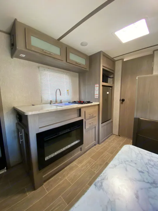 Explore this RV rental's inviting kitchen area, complete with sink, stove, fridge, fireplace, and light wood cabinetry.. Dutchmen Coleman Lantern LT 2022