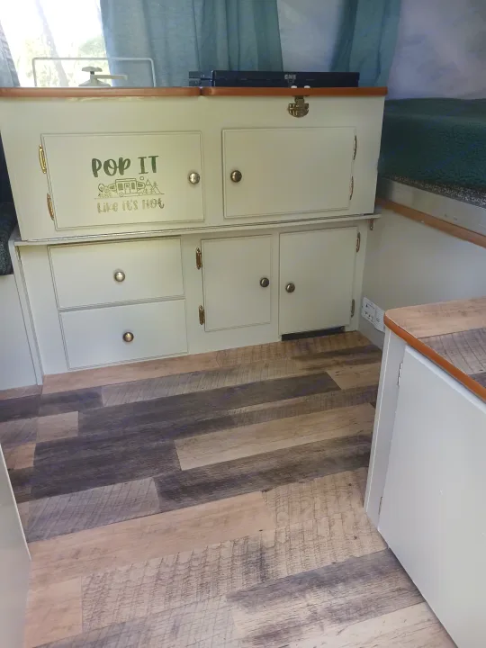 This inviting RV rental interior showcases custom light-colored cabinets, wood-look flooring, and a playful 'POP IT' graphic.. Coleman Other 2002