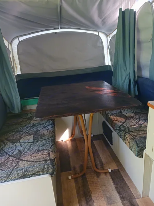RV rental: Inside a pop-up camper featuring a dark wooden table, patterned benches, and light fabric walls.. Coleman Other 2002