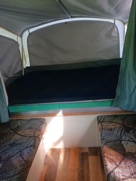 Pop-up RV rental interior: featuring a comfortable bed, patterned seating, and wood-look flooring.. Coleman Other 2002