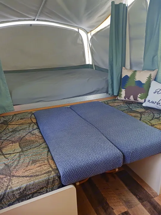 RV rental interior: a comfy bed, blue cushions, and a bear pillow in a cozy pop-up camper.. Coleman Other 2002
