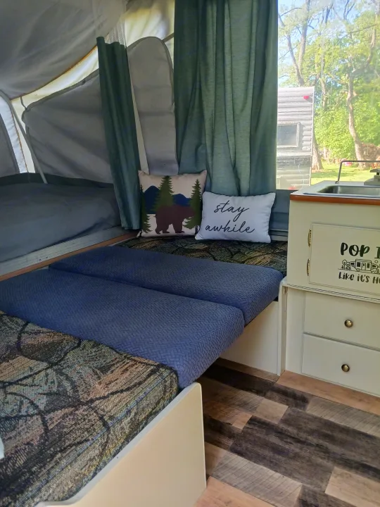 Step into this cozy pop-up camper RV rental, featuring beds with patterned cushions, decorative pillows, and a compact sink area.. Coleman Other 2002