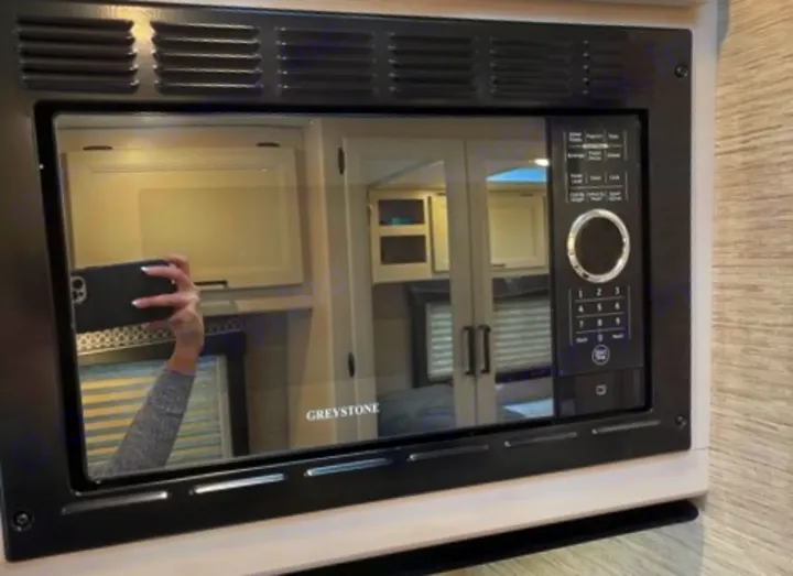 Sleek black Greystone microwave in an RV rental. Reflection shows a person taking the photo with a phone.. Thor Motor Coach Four Winds 2022