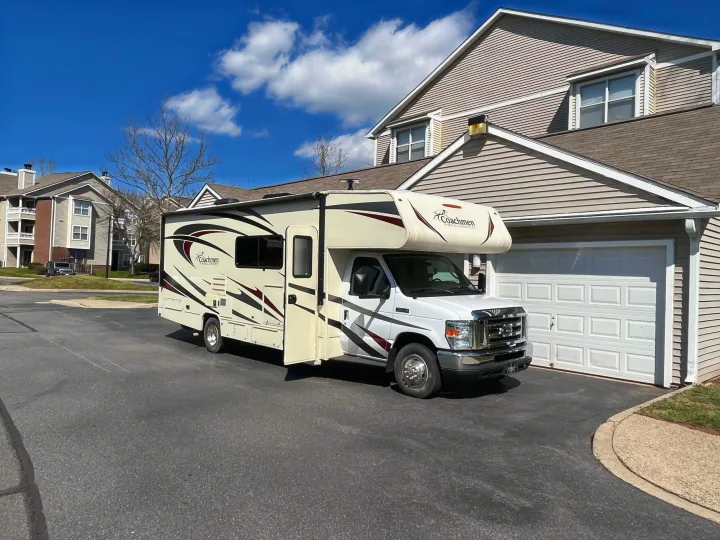 A white Coachmen Freelander Class C RV rental, with an open side door, is parked on asphalt by a garage.. Forest River Coachmen Freelander 2018