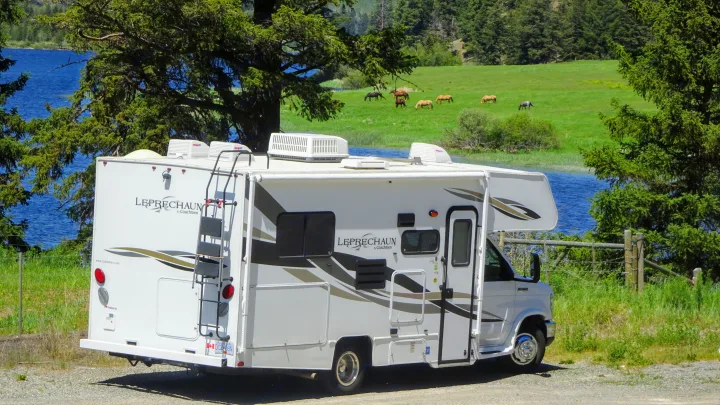 White Coachmen RV rental parked by a lake, providing scenic views of water and horses grazing in a green field.. Forest River Coachmen Leprechaun 2014