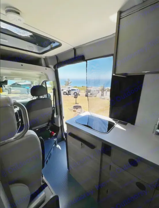 Explore this RV rental's cozy camper van interior with kitchenette, seats, and stunning ocean view from a sunny campsite.. Winnebago SOLIS 59 PX 2023