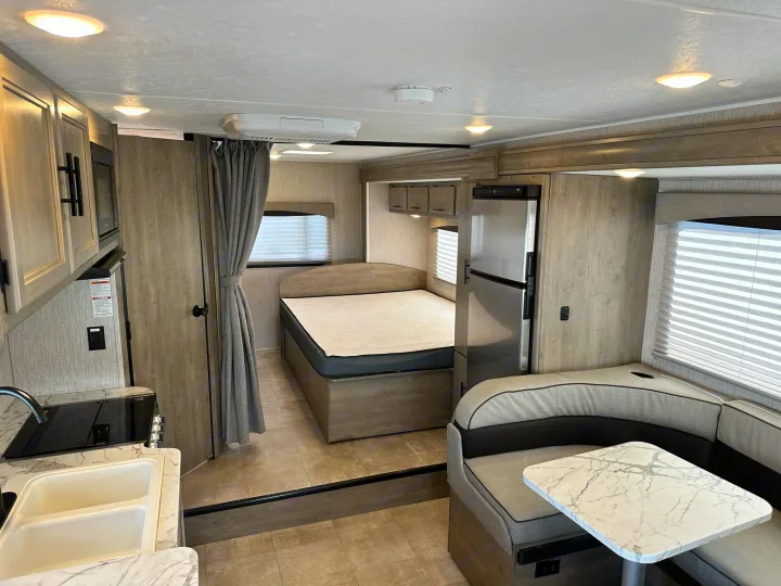 RV rental interior: a compact kitchen, bed area with curtain, L-shaped dinette, and refrigerator. Light wood finishes.. Coachmen Freelander 2022