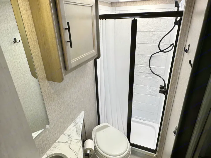 Modern RV rental bathroom featuring a shower, toilet, vanity, and overhead cabinet.. Coachmen Freelander 2022