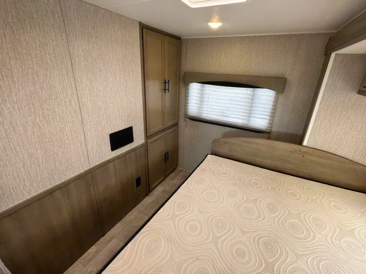 Cozy RV rental bedroom featuring a bed, ample cabinets, and a window with blinds, showing a compact living space.. Coachmen Freelander 2022