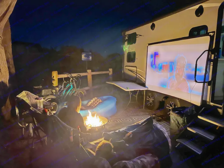 Relaxing RV rental night: campfire, outdoor movie projected beside the RV, with people enjoying the cozy evening.. Keystone RV Bullet Ultra Lite 2020
