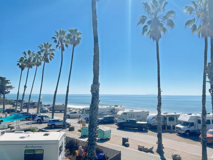 Bright coastal RV park scene featuring numerous motorhomes and travel trailers (great for RV rental vacations) parked by the sunny ocean with palm trees.. Keystone RV Bullet Ultra Lite 2020
