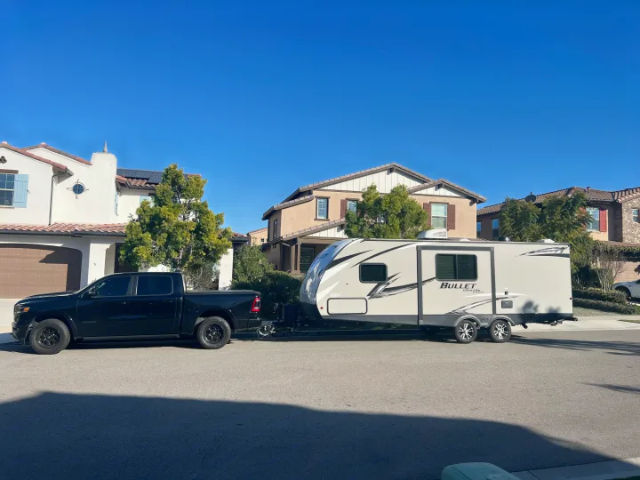 A black truck is hitched to an RV rental, a Bullet Ultra Lite travel trailer, parked on a sunny residential street.. Keystone RV Bullet Ultra Lite 2020
