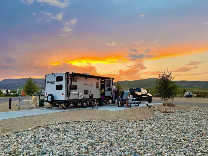 A family enjoys a vibrant sunset at their RV rental campsite, featuring a modern travel trailer, truck, and peaceful dog.. Keystone RV Bullet Ultra Lite 2020