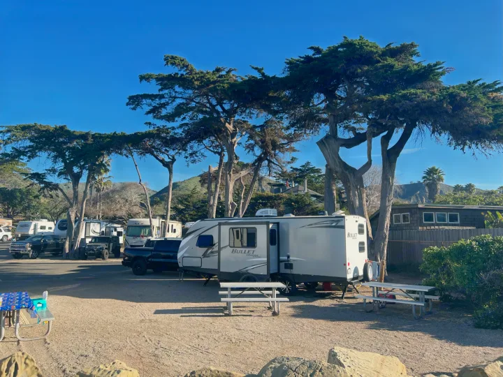 A sunny campground scene with various RVs, including a modern Bullet travel trailer for potential rv rental, under a clear blue sky.. Keystone RV Bullet Ultra Lite 2020