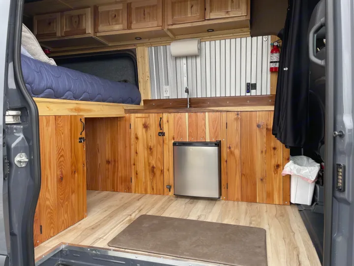 Spacious RV rental van conversion with custom wooden cabinetry, a bed, and kitchenette.. Mercedes Sprinter 2022