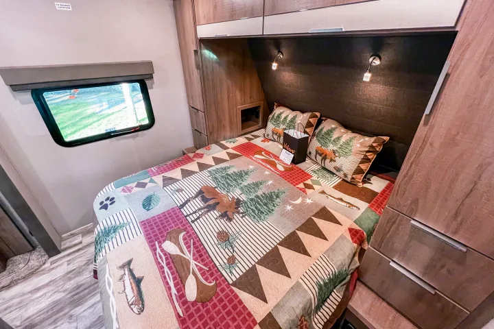 Explore comfort in this RV rental bedroom featuring a rustic nature-themed quilt, cozy reading lights, and ample storage.. Grand Design Reflection 2021