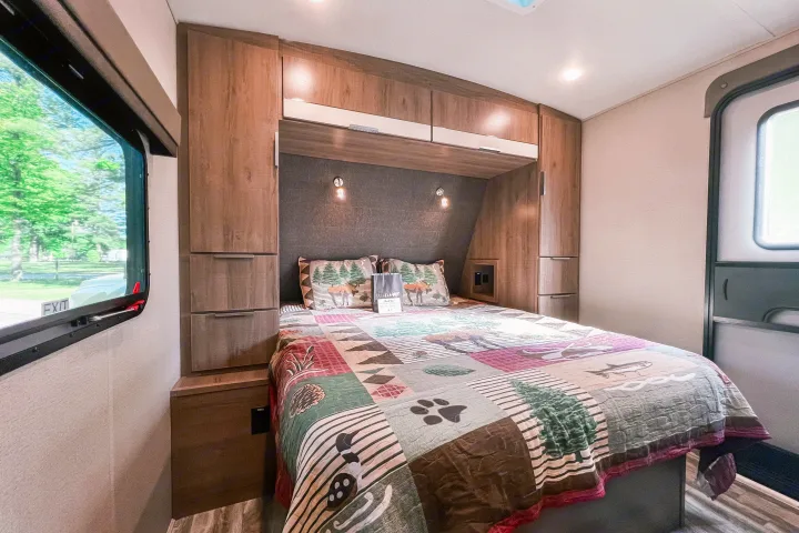 Inside a cozy rv rental, this bedroom offers a comfy bed with nature-themed bedding, storage, and a window view.. Grand Design Reflection 2021