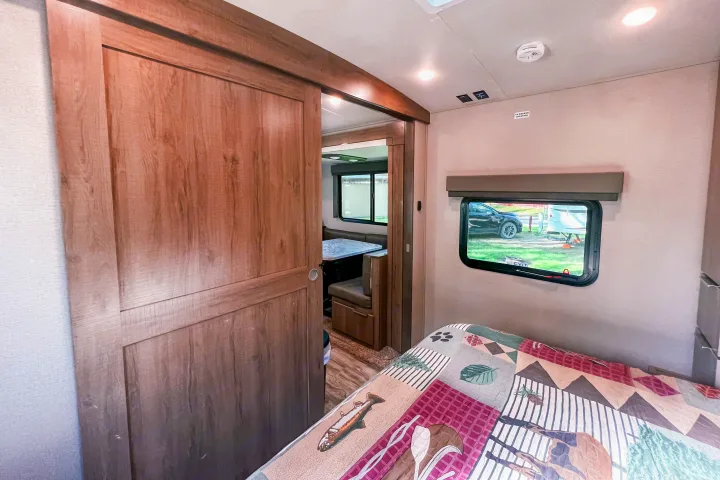 Cozy RV rental bedroom with patterned quilt, sliding door reveals dinette. Ideal for comfortable travel.. Grand Design Reflection 2021
