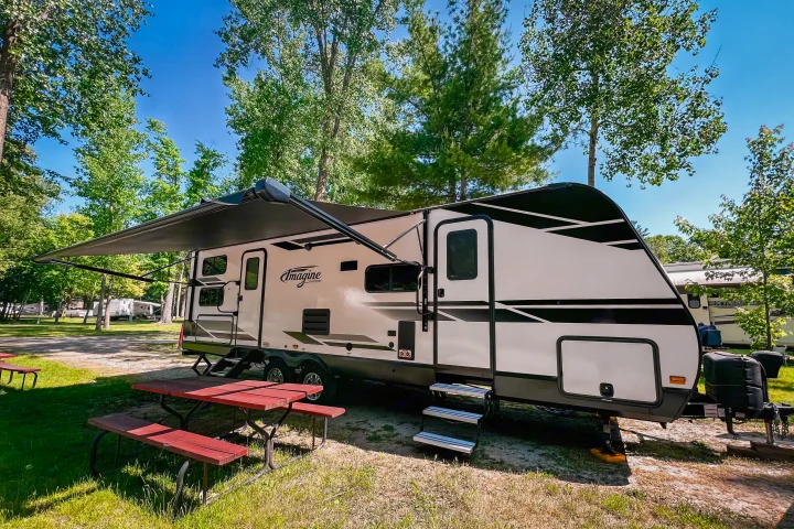 RV rental travel trailer parked on a sunny campground campsite with an extended awning and red picnic table.. Grand Design Reflection 2021
