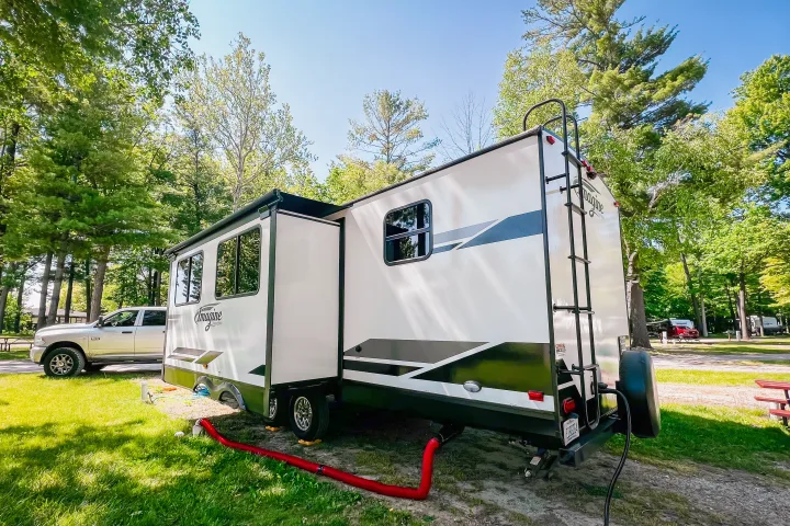 White Imagine RV rental travel trailer with extended slide-out, parked at a treed campsite with a white pickup truck.. Grand Design Reflection 2021