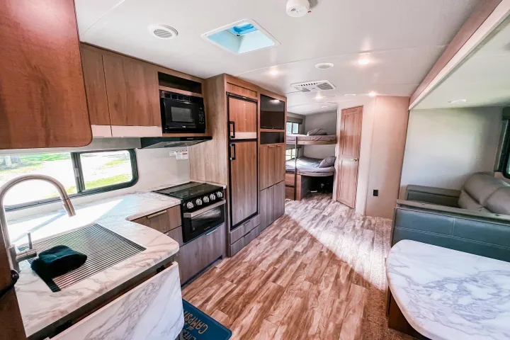 Spacious RV rental interior featuring a modern kitchen, living area with sofa, and rear bunk beds.. Grand Design Reflection 2021