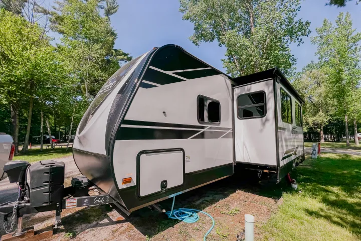 Enjoying a serene RV rental experience: a modern travel trailer parked among green trees in a sunny campground.. Grand Design Reflection 2021