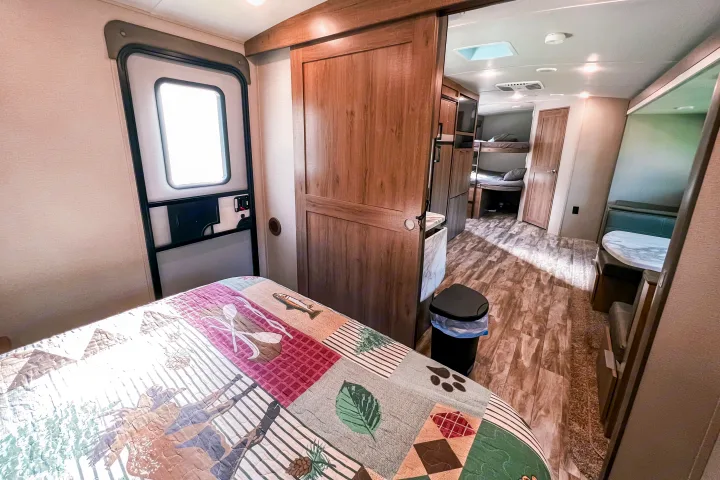 Bright RV rental interior with a cozy bed, bunk beds, kitchen, and dining booth. Ideal for a family camper getaway.. Grand Design Reflection 2021