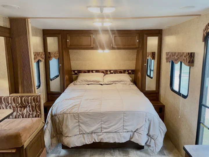Cozy RV rental bedroom featuring a large bed, built-in cabinets, and dual windows. Perfect for comfortable travel.. Sportsmen Show Stopper 2016