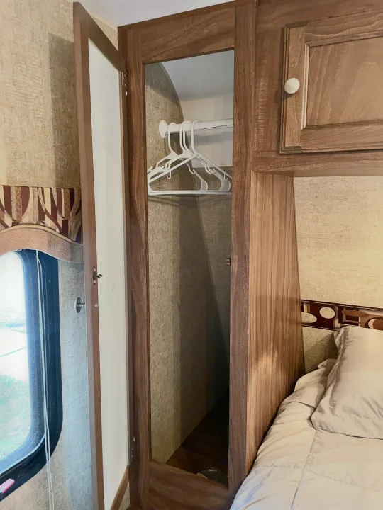 RV rental interior: Open wardrobe with hangers, adjacent bed, window with valance. Compact and functional storage.. Sportsmen Show Stopper 2016