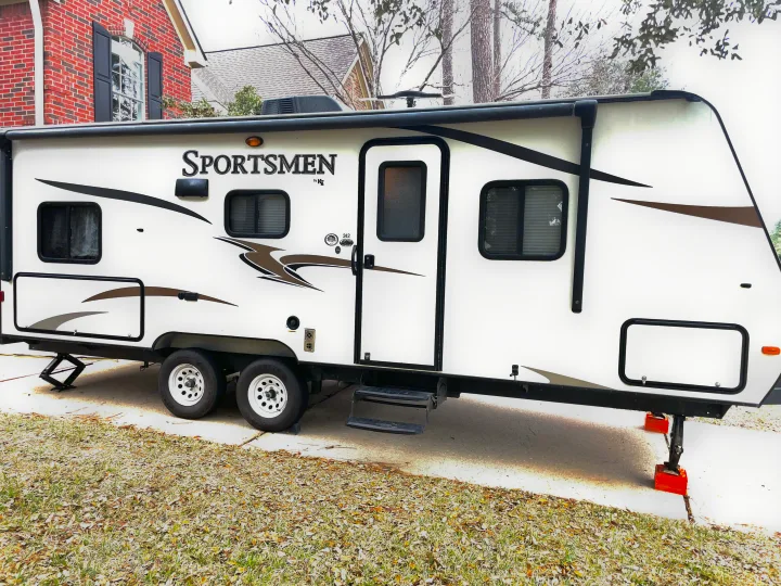 White Sportsmen travel trailer, a spacious RV rental option, parked on concrete with leveling jacks deployed.. Sportsmen Show Stopper 2016