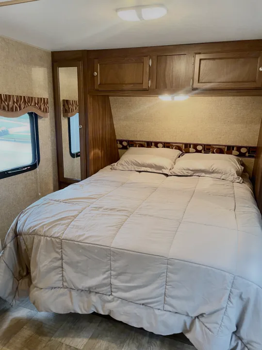 Inviting RV rental bedroom with a comfortable bed, overhead cabinets, mirrored closet, and window. Ready for your trip!. Sportsmen Show Stopper 2016