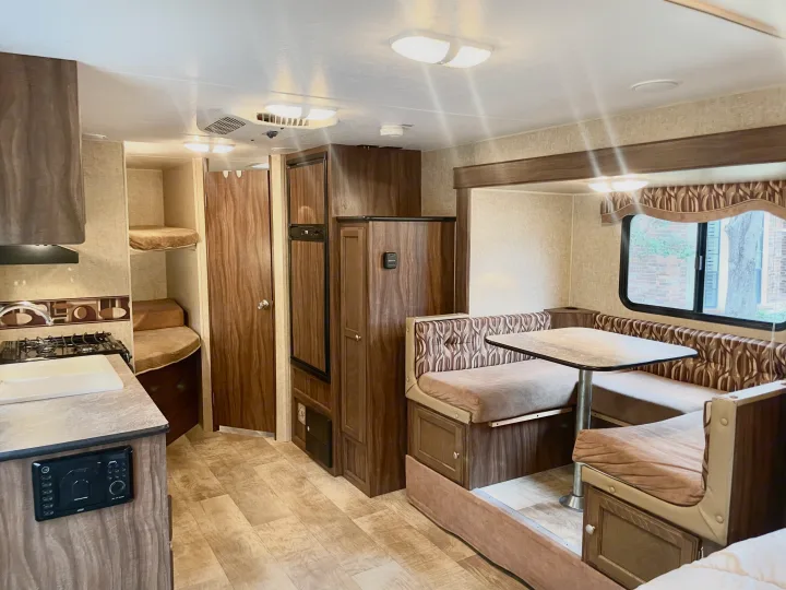 RV rental interior featuring a cozy dining booth, compact kitchen with sink and stove, and bunk beds, perfect for family adventures.. Sportsmen Show Stopper 2016