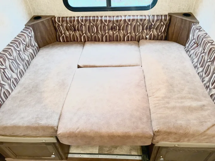 Comfortable RV rental interior showing a dinette converted to a cozy bed with patterned cushions and cupholders.. Sportsmen Show Stopper 2016