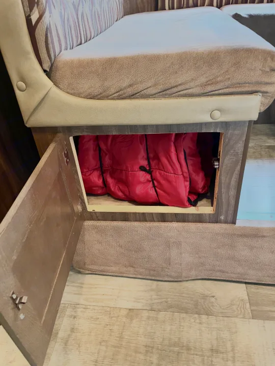 RV rental storage: Open compartment under bench seat reveals neatly packed red sleeping bags, ideal for trips.. Sportsmen Show Stopper 2016