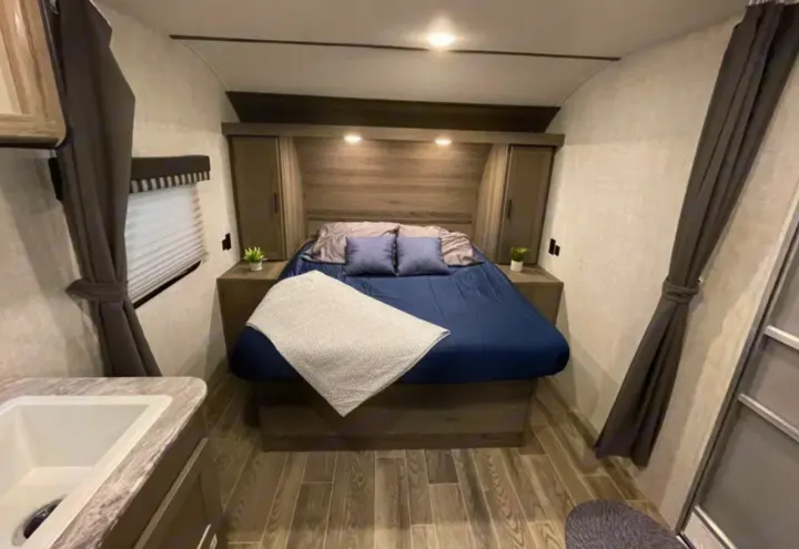Inviting RV rental bedroom with comfortable bed, built-in storage, and convenient sink area. Perfect for travel.. Grandriver 25BH 2021