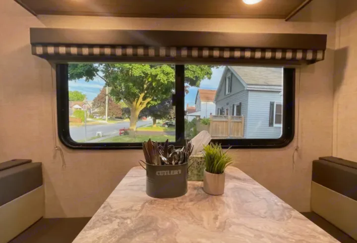 Bright RV rental dining area with a street view through the window, featuring a large table and benches.. Grandriver 25BH 2021