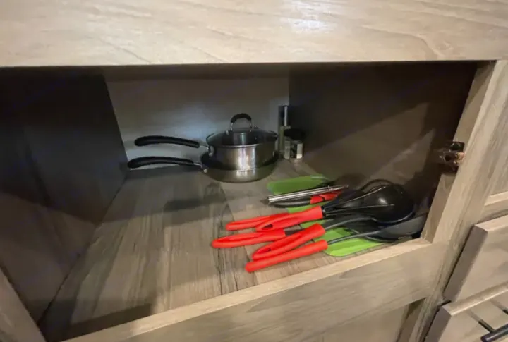 RV rental kitchen cabinet with stacked pots, pans, and red-handled utensils, plus spices, for compact cooking.. Grandriver 25BH 2021