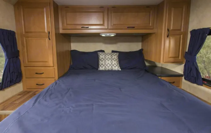 A cozy RV bedroom for your next rv rental adventure, featuring a bed with blue bedding, storage cabinets, and natural light.. Thor Majestic 2018