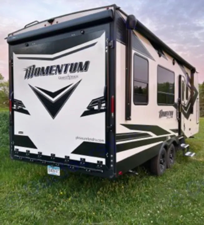 Get ready for adventure! This white/black Momentum G-Class toy hauler RV rental is parked in grass, ready for your next road trip.. Grand Design Momentum 2022