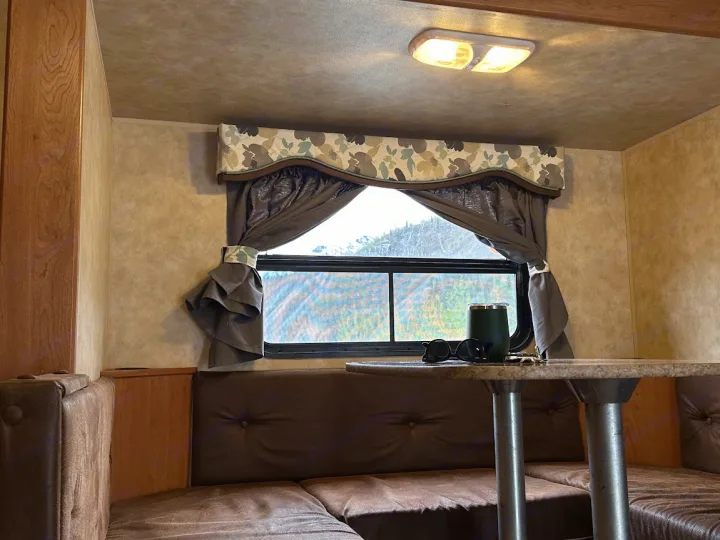 Relaxing RV rental interior with a brown leather dinette, window view, and table holding a mug & sunglasses.. KZ Sportsmen 2009