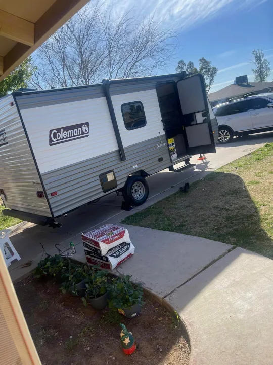 This Coleman travel trailer RV rental, open and parked on a sunny driveway, is ready for camping adventures and outdoor gear.. Coleman Lantern LT 17B 2023