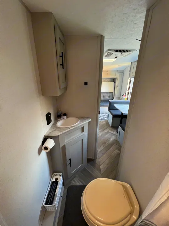 RV rental bathroom and living area: Features a compact toilet, sink, and dinette with herringbone flooring.. Forest River Wildwood FSX 2021