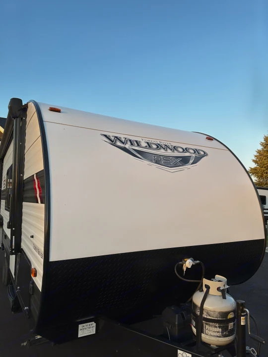 Bright blue sky over a white Forest River Wildwood FSX travel trailer, featuring a propane tank, ready for rv rental.. Forest River Wildwood FSX 2021