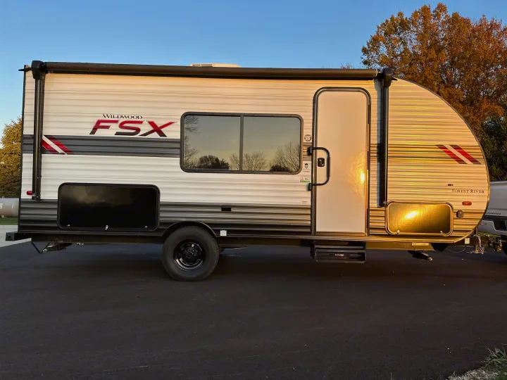 Wildwood FSX Forest River travel trailer, a compact RV rental, parked on asphalt in sunlight.. Forest River Wildwood FSX 2021
