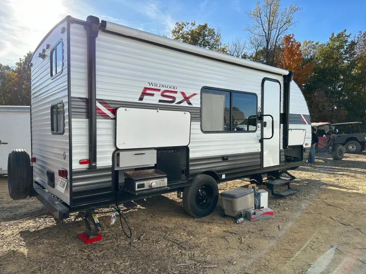 Wildwood FSX RV rental travel trailer with an outdoor kitchen and rear spare tire, parked on dirt.. Forest River Wildwood FSX 2021