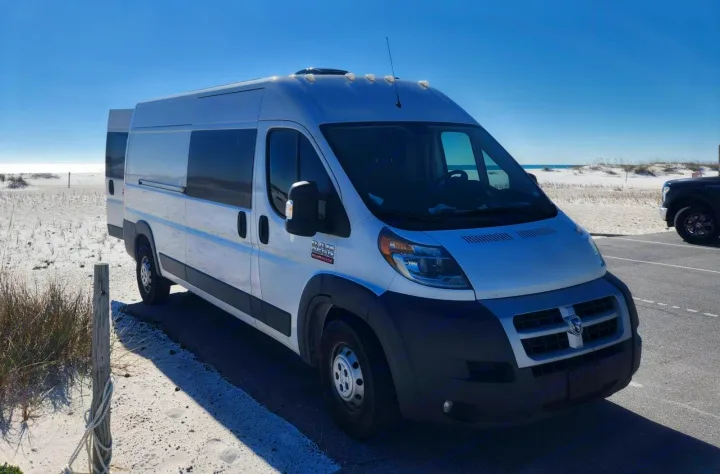 White RV rental camper van parked on a sunny beach road, with sandy dunes and ocean visible in the background.. Dodge 1500 2014